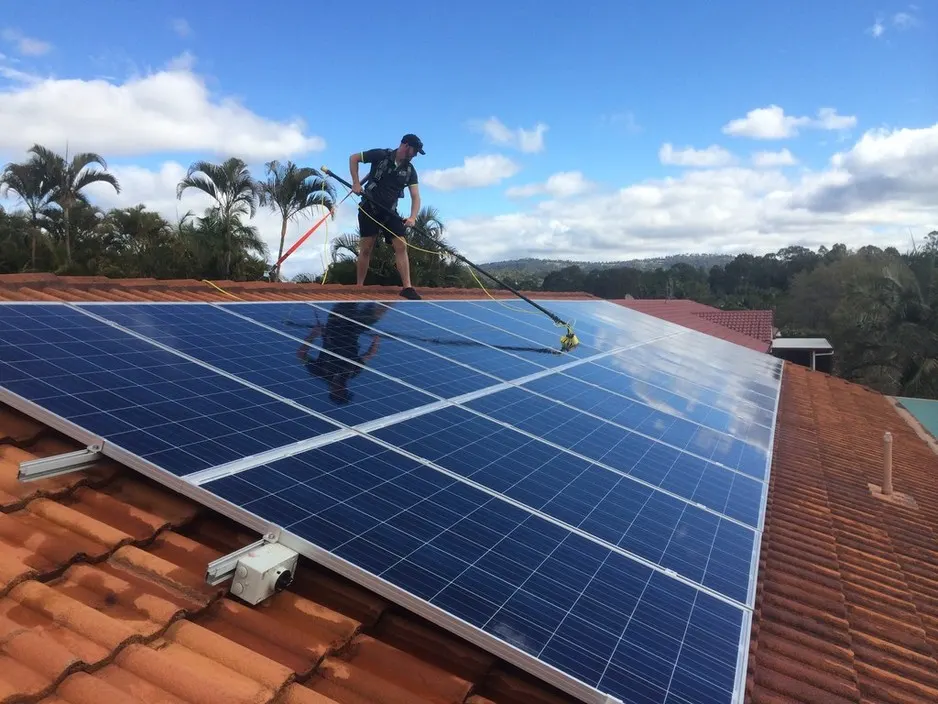 Técnico limpando painéis solares em um telhado